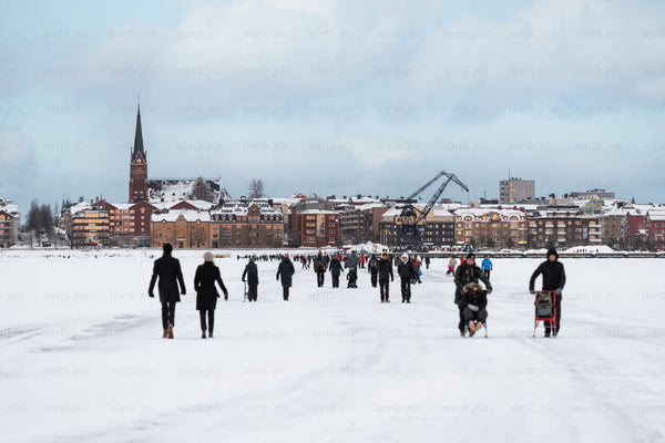 People walking on frozen river toward town skyline