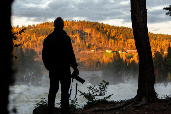 Photographer at riverside rapids at sunset, autumn