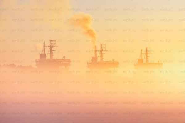 Three icebreakers in fog at sunrise