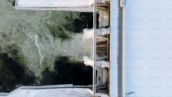 Hydroelectric power station dam in winter: An aerial view of flowing water and snow