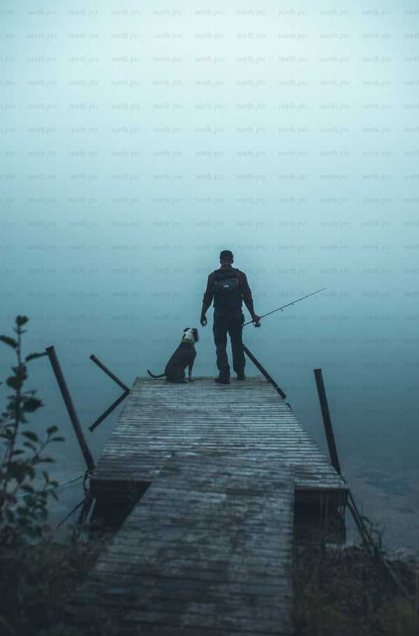 Man fishing with dog on wooden dock in fog