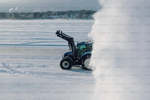 Blue tractor clearing snow in open field with large snow cloud in winter landscape