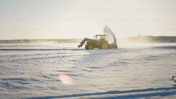 Tractor clearing snow on frozen lake in Luleå during golden hour