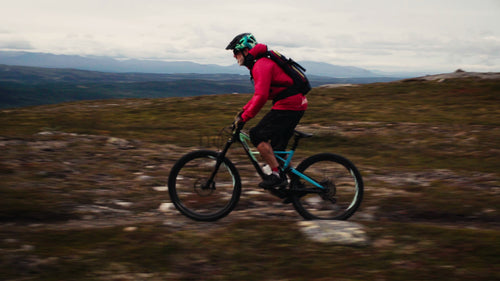 Mountainbiker i röd jacka som cyklar nedför en stenig sluttning