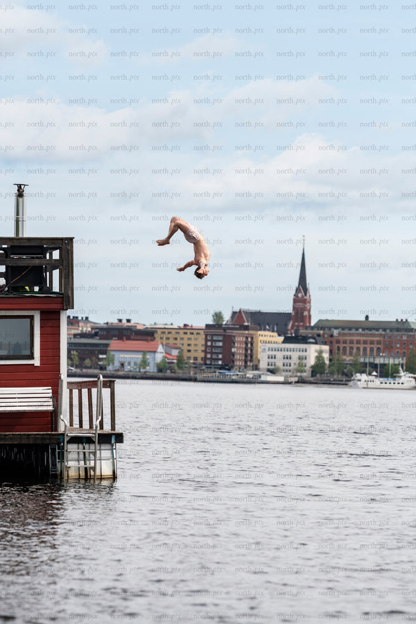 Man diving from dock over water with city skyline, daytime