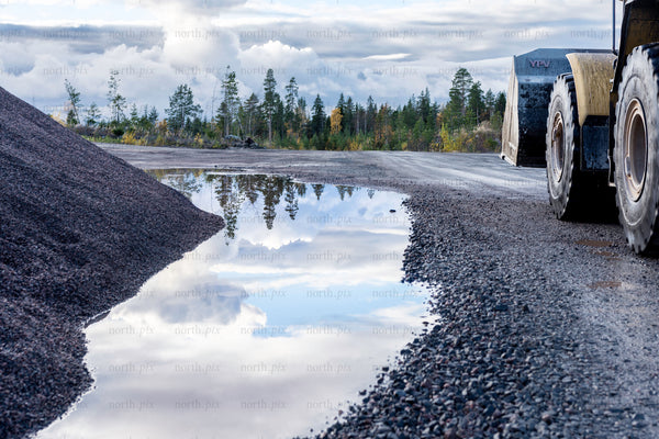 Wheel loader and gravel pile on wet gravel road, autumn