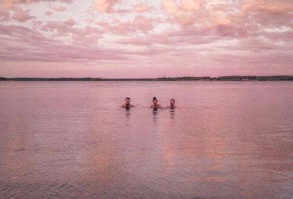 Three people swimming in lake at sunset