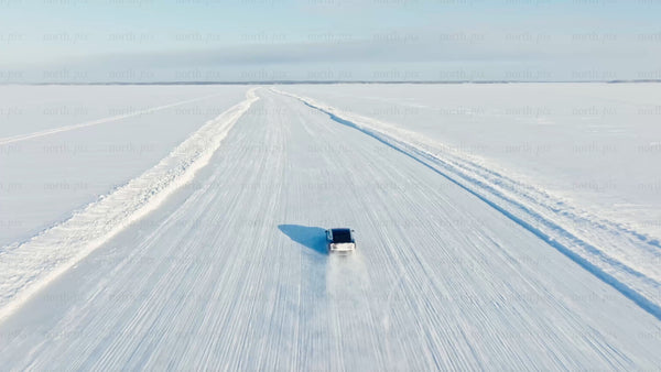 White Tesla/car driving on snowy ice road in Luleå, winter day, drone shot