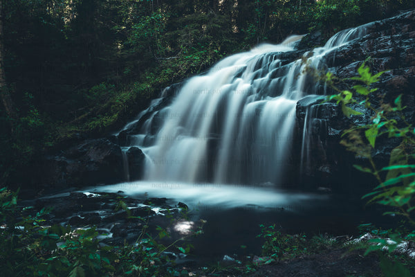 Multi-tiered waterfall flowing over rock ledges in forest