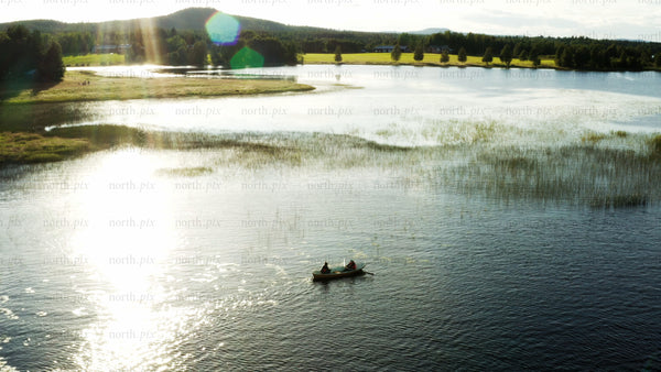 Two people rowing a boat on a calm lake at sunset in Luleå