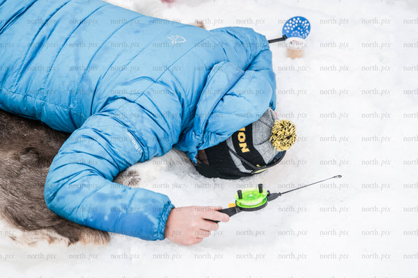 Person ice fishing on snow in winter wearing blue jacket