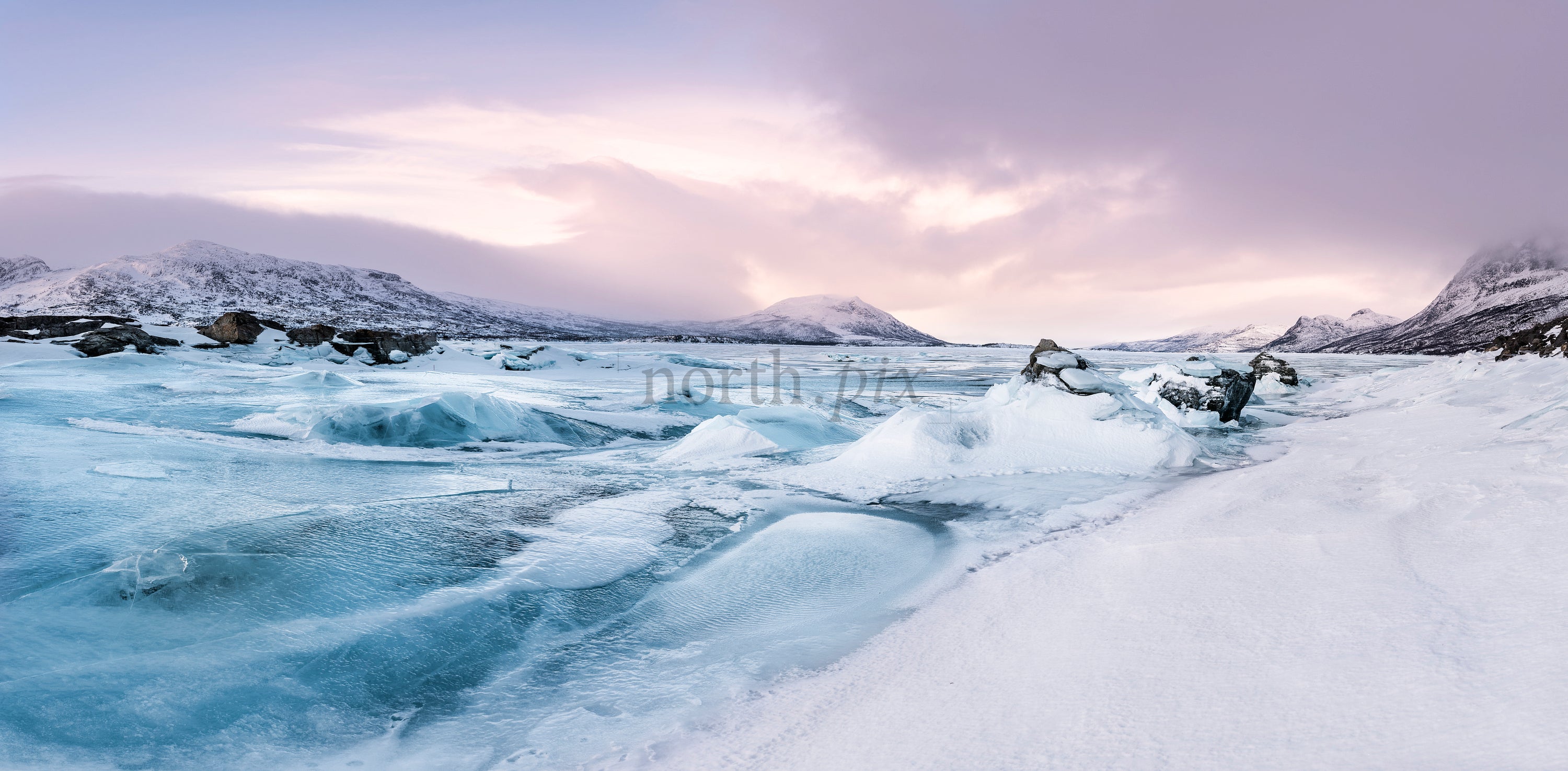 Panoramic frozen lake and snow-covered mountains at sunrise