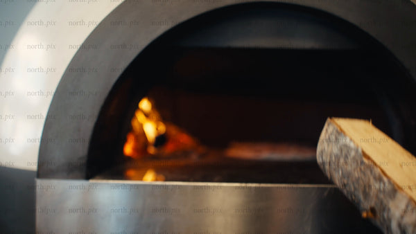 Chef adds wood to fire in brick oven while baking pizza: Slow motion close-up