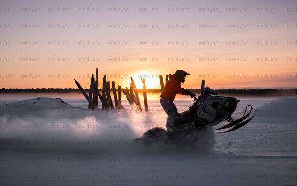 Snowmobile rider on a frozen lake at sunset