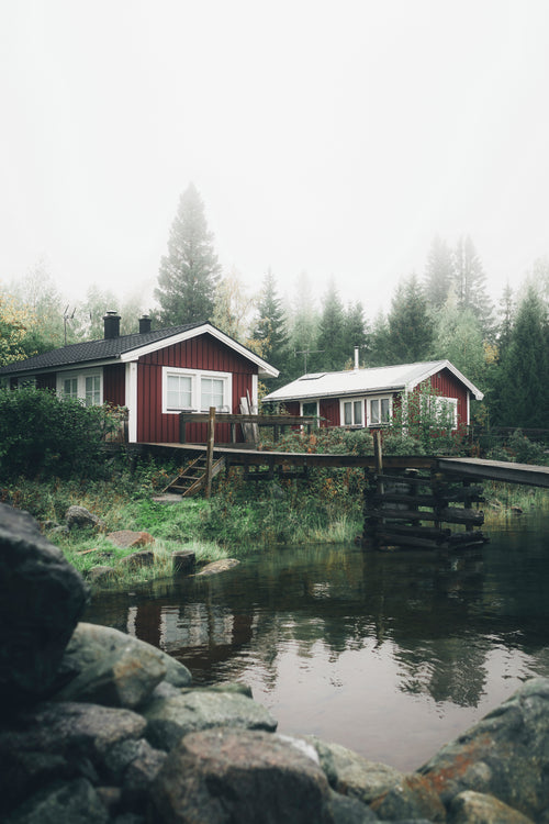 Röda trästugor vid sjö med brygga och skog