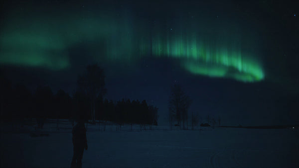 Person walking on a frozen lake under northern lights
