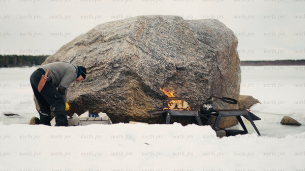 Winter cooking in the Luleå archipelago: Man prepares a meal by a campfire on a frozen lake