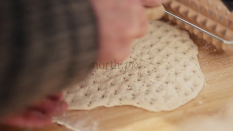 Hands Imprinting Dough with Patterned Rolling Pin on Wooden Board
