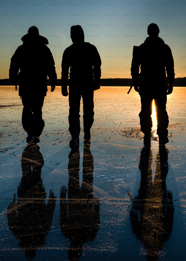 Three people walking on frozen lake at sunset