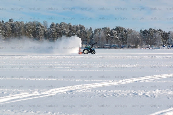 Winter snow field with tractor clearing snow on frozen lake near Luleå city center