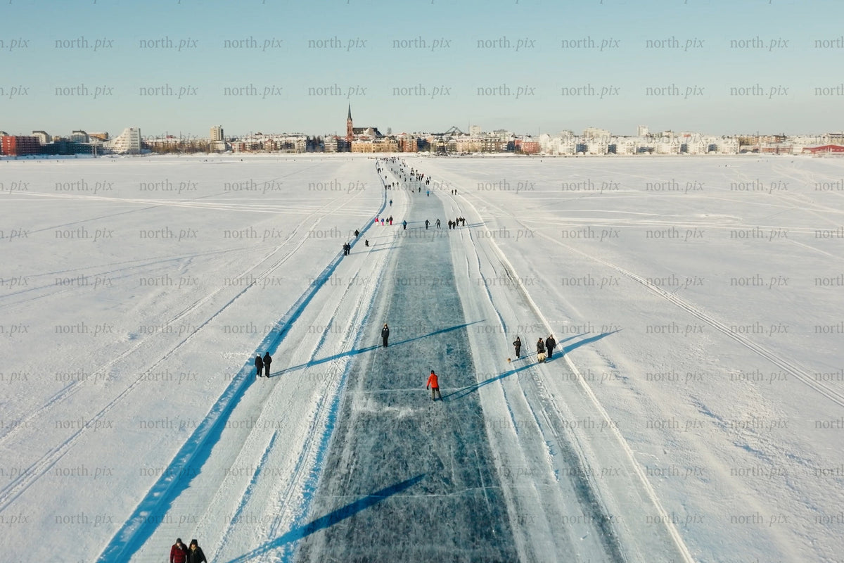 Isstig över snötäckt sjö mot Luleå centrum med åkare och snötäckt skyline