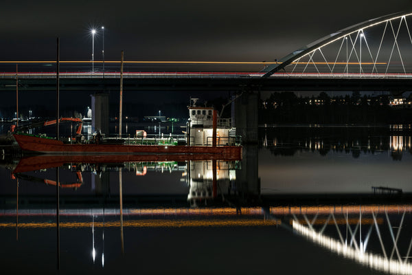 Cargo boat moored under illuminated bridge at night
