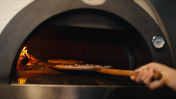 Chef places pizzas in wood fired oven in restaurant kitchen