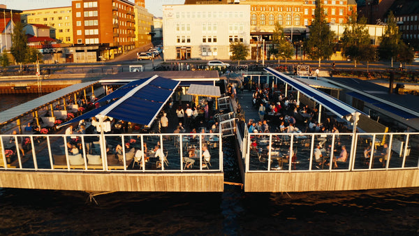 Luleå: Summer sunset over city harbor with people enjoying drinks at floating restaurant