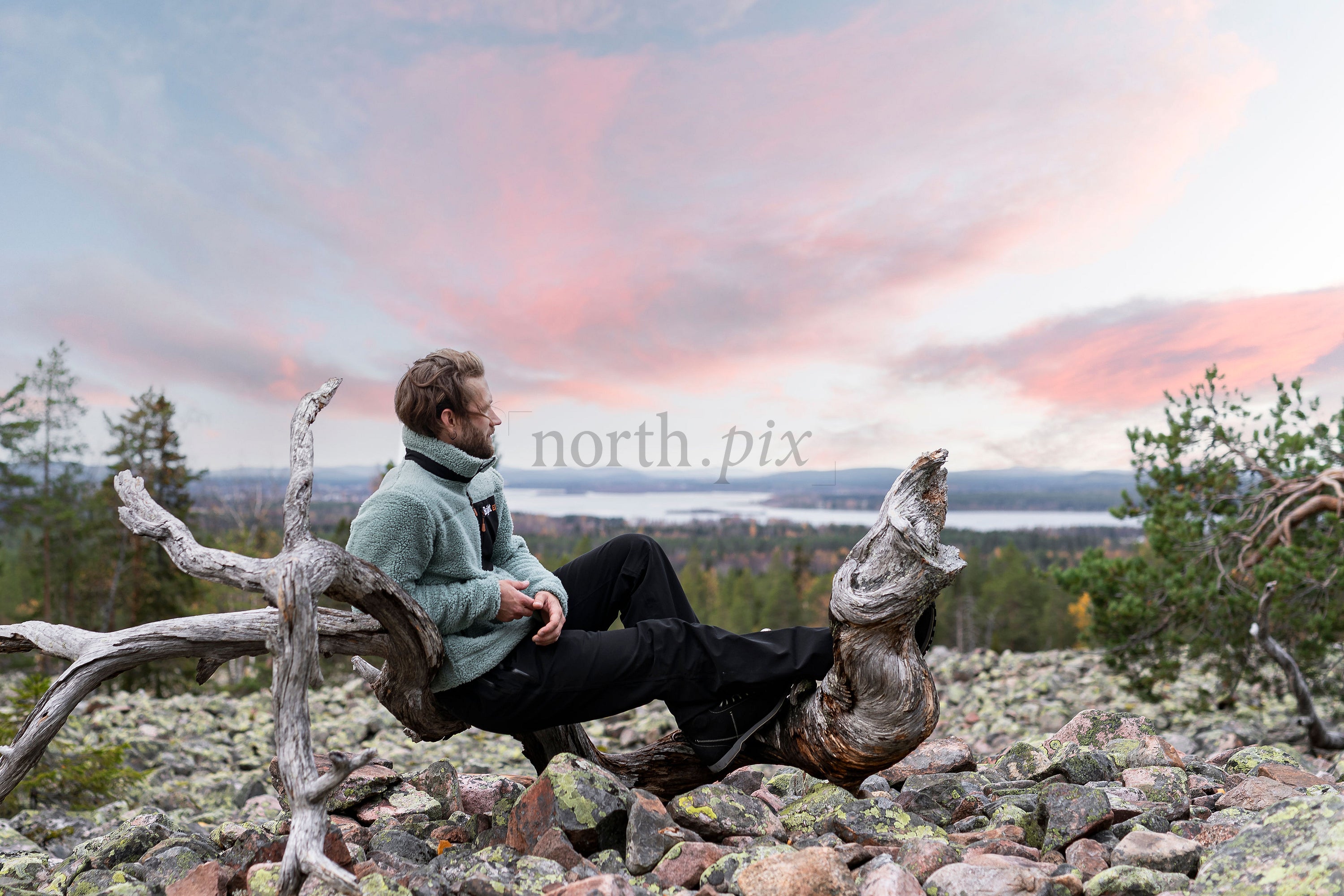 Man sitting on dead tree above rocky hill at sunset