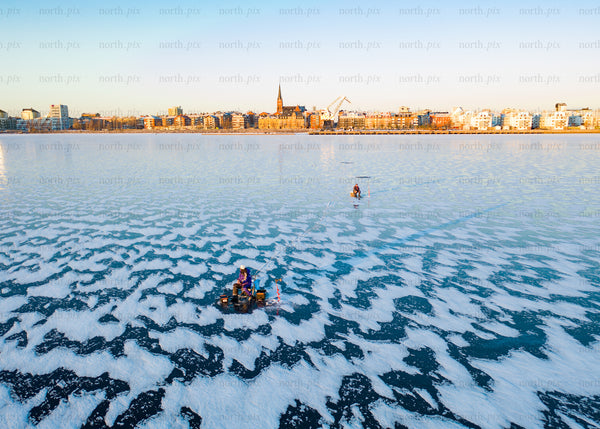 Winter cityscape view of frozen lake with people in morning light