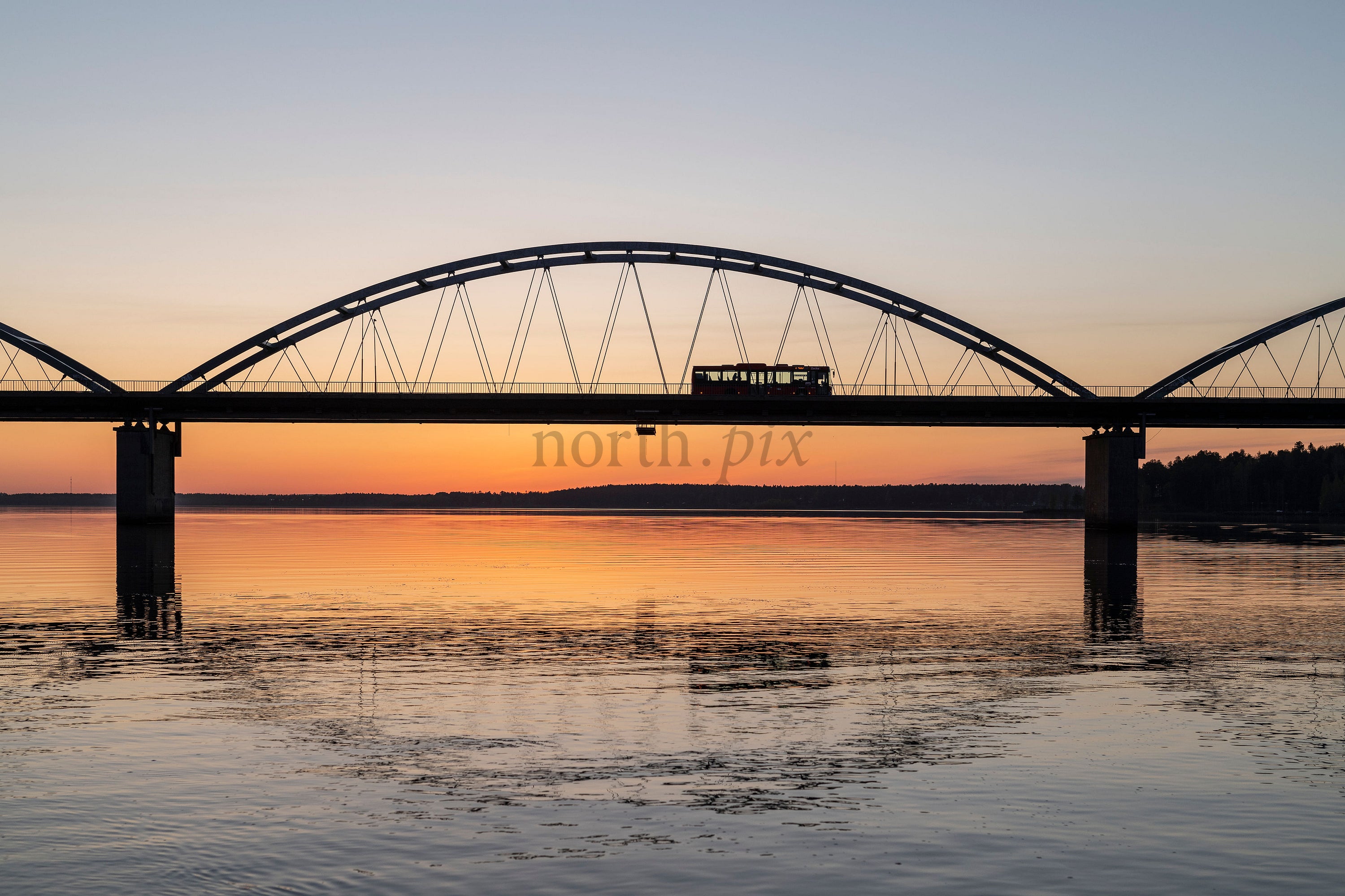 Tram crossing arch bridge over river at sunset