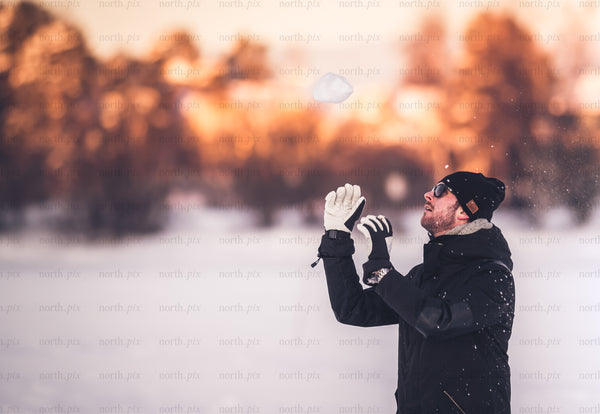Man tossing snow in winter field at sunset