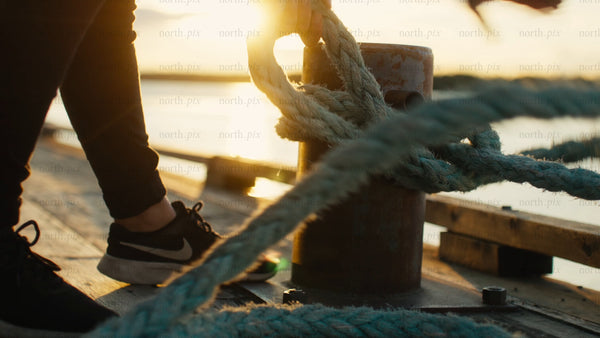 Sunset over water, rope tied to mooring on wooden dock, Luleå