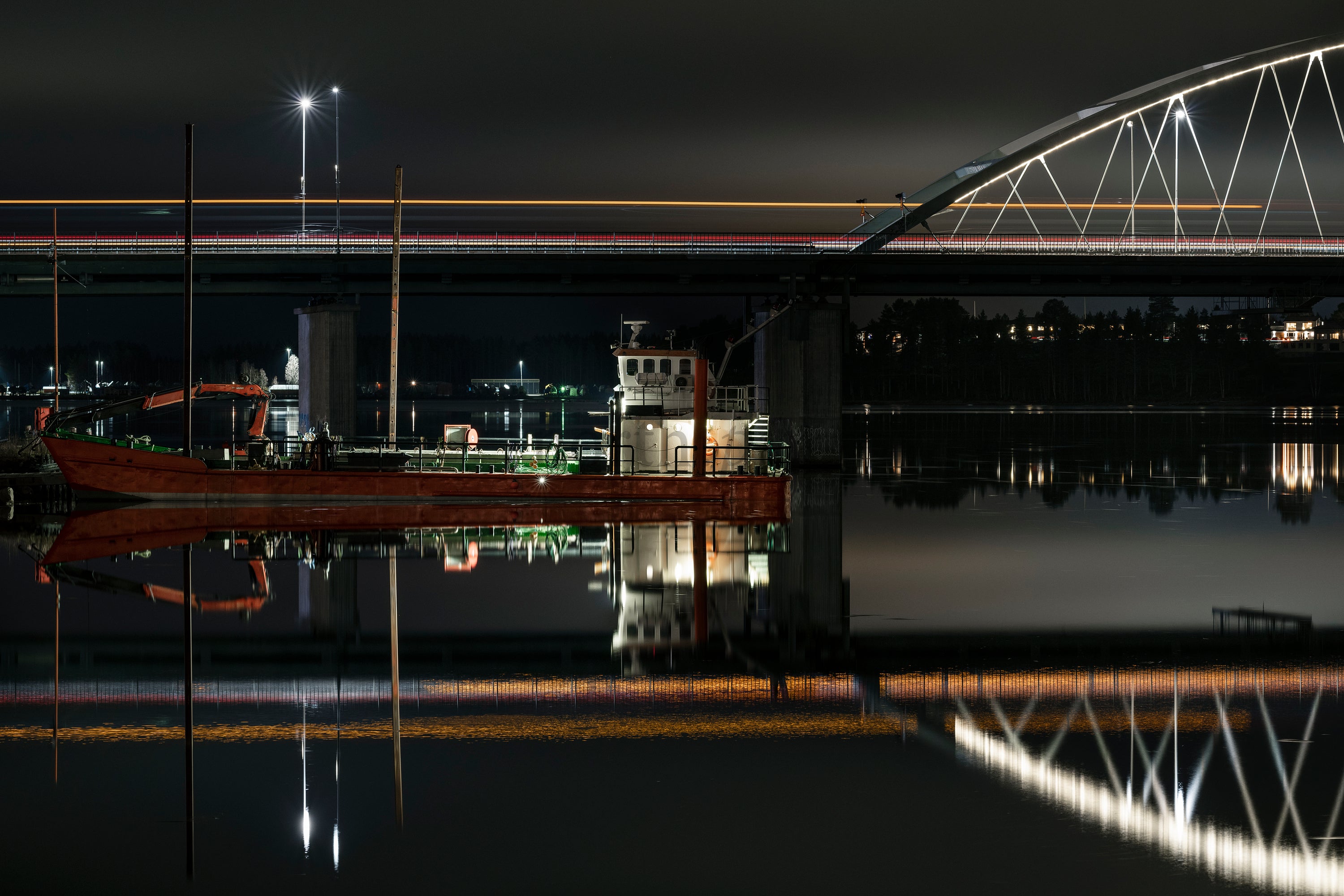 Red workboat moored under illuminated modern bridge at night