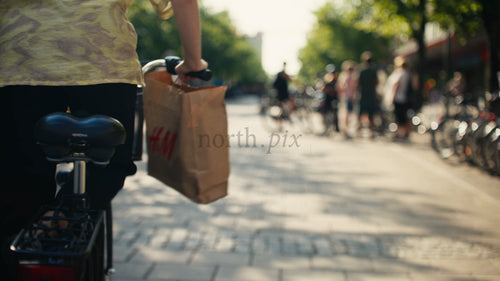 Kvinna cyklar genom solig stadsgata med shoppingkasse i Luleå, Sverige