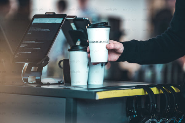 Person grabbing takeaway coffee at cafe counter