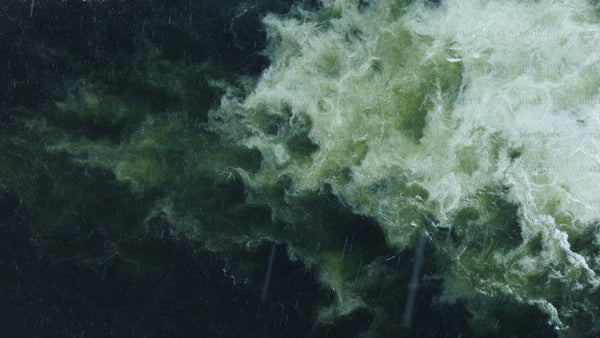 Top down aerial view of swirling water flow with teal and green in the rain