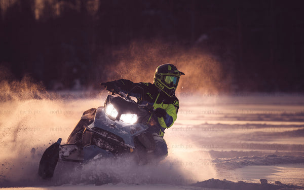 Snowmobile rider on snowy field at sunset