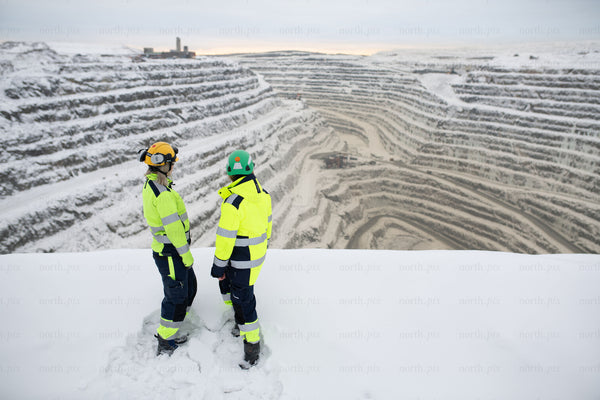 Two workers overlooking snowy open pit mine in winter