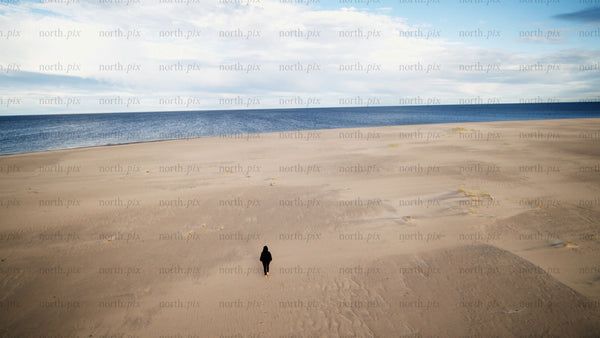 Lone person walks on sandy beach toward ocean in Luleå, summer day drone shot