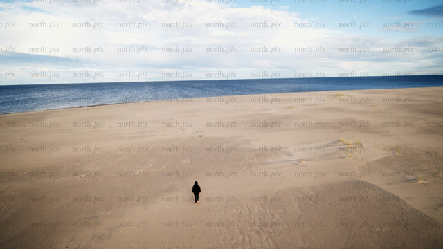 Lone person walks on sandy beach toward ocean in Luleå, summer day drone shot