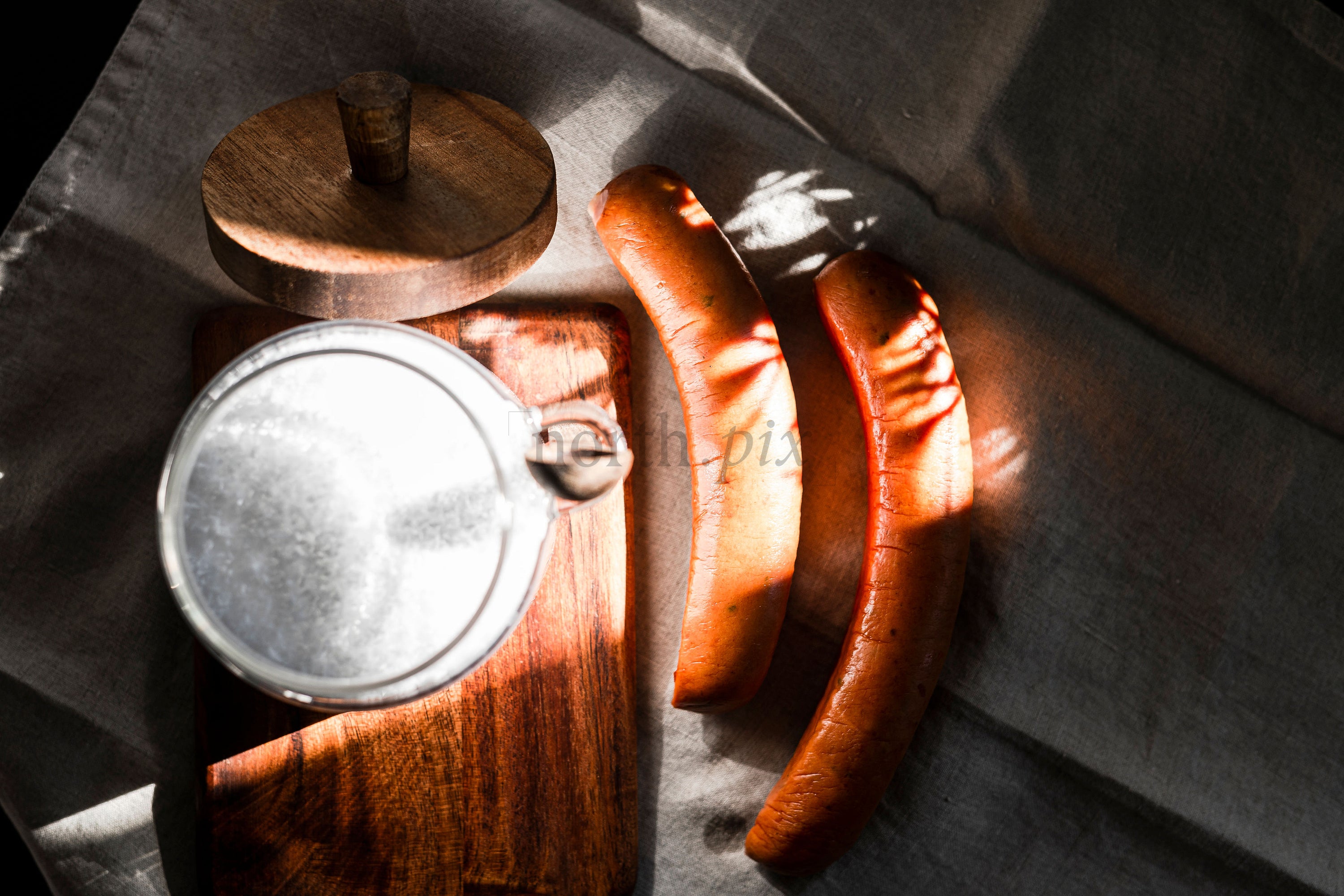 Sausages and milk jar on wooden board, morning light