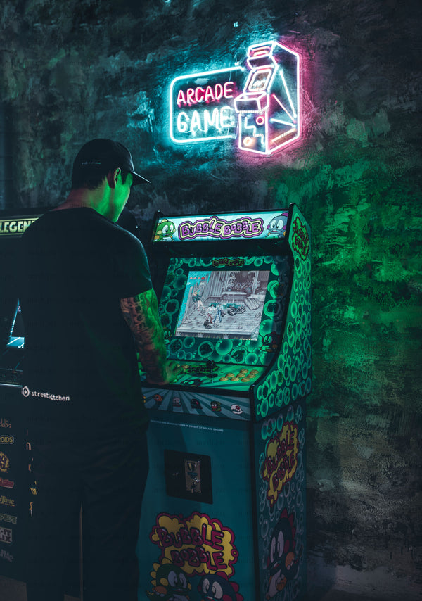 Man playing arcade game cabinet under neon sign