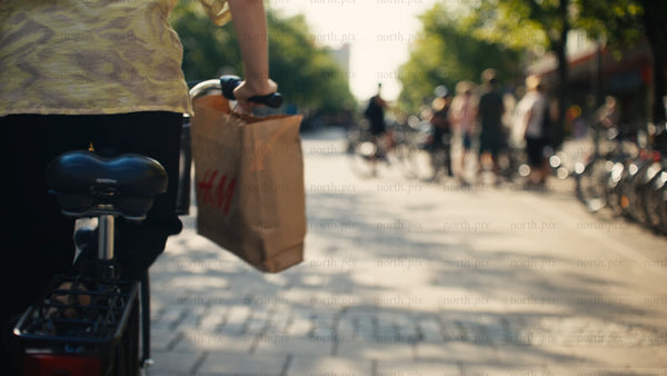 Woman cycles through sunny city street with shopping bag in Luleå