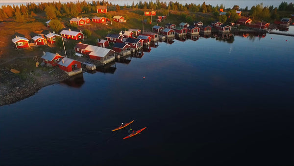 Kayakers paddle past red cabins in the Luleå archipelago at sunset