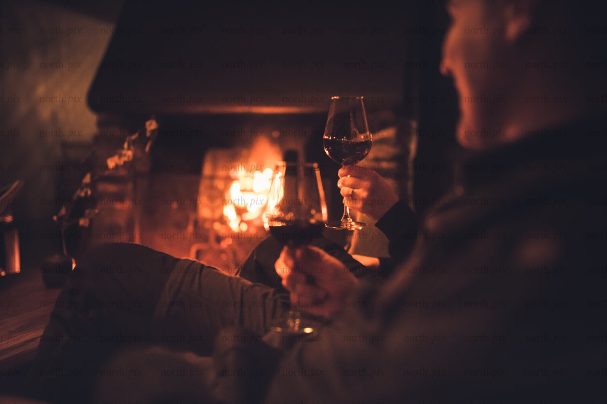 Two people holding wine by a fireplace at night