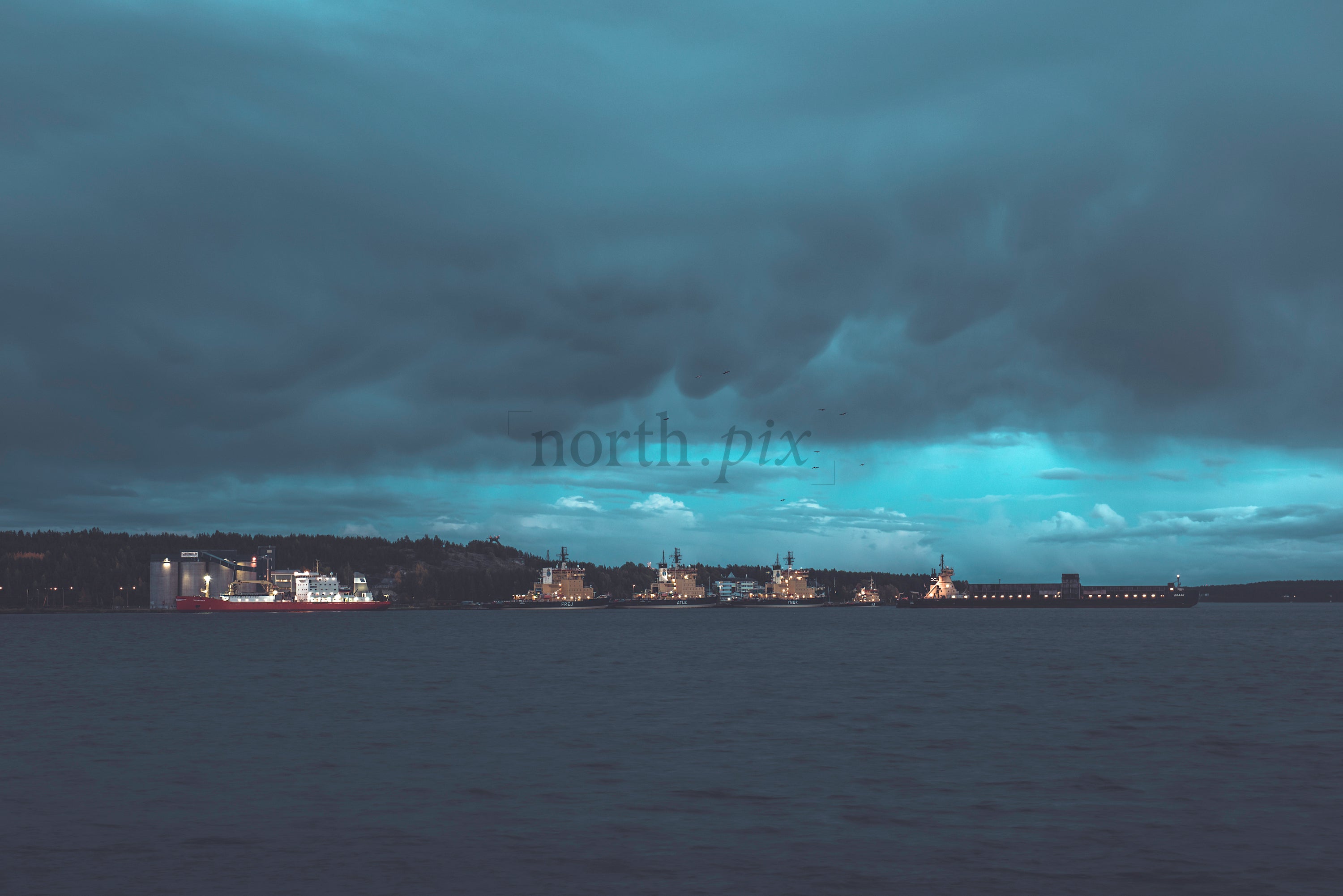 Cargo ships moored at harbor under heavy clouds