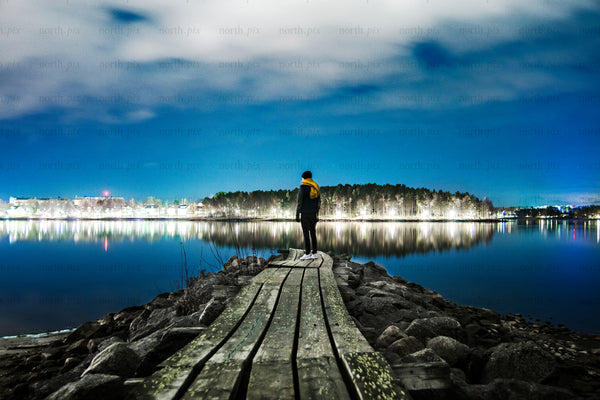 Man standing on wooden pier at night by lake