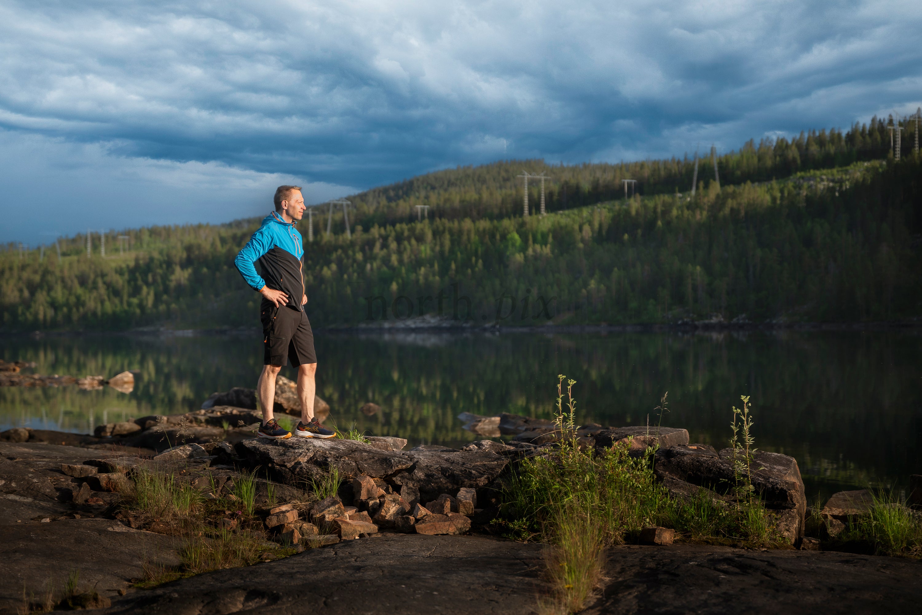 Man standing on rocky lakeshore at dusk, summer