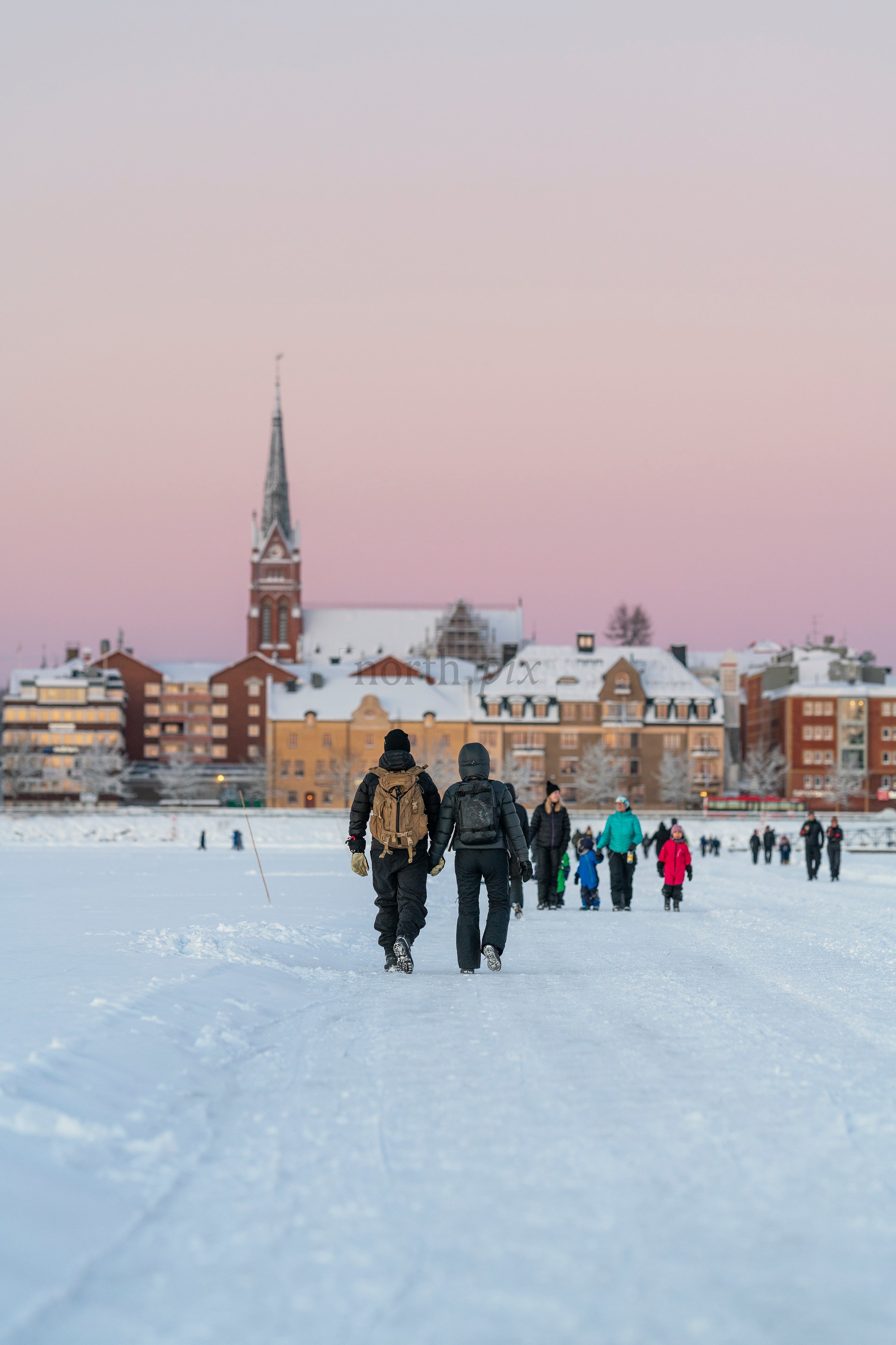 Two people walking on ice road toward snowy city